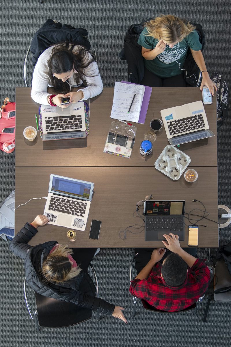 Four students studying around a table with laptop computers open.